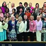 Group photo of women at a community event in a hall, smiling and posing together on multiple levels.