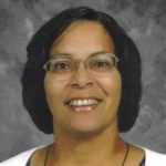 I'm unable to identify individuals in images. However, here’s an example of an alt text you could use: Person wearing glasses smiling against a gray backdrop.