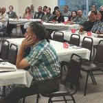 Attentive audience at a training workshop, seated at tables with notebooks and decorations.