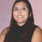Smiling woman with long hair and black top against a soft pink background, showcasing a professional and friendly demeanor.