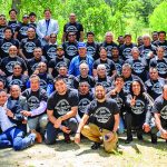 Group photo of people outdoors, wearing matching shirts, during a team-building event in a green park setting.