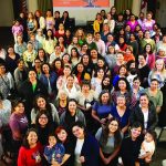 Diverse group of women at a community gathering in a hall with a banner in the background.