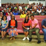 A diverse group of people seated in a church setting, smiling and posing for a community gathering photo.