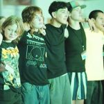 A diverse group of young people standing together with arms around each other, displaying friendship and unity.