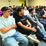 Audience attentively listening at an indoor event, seated in rows of chairs.