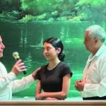 A group of four people engaged in conversation with a green lit backdrop, featuring a man holding a microphone.