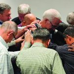 A group of men huddled, engaging in a heartfelt prayer or meeting, conveying unity and support.