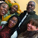 A group of five smiling people taking a selfie at a gathering, with colorful attire and a friendly atmosphere.