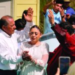 A woman being baptized in an outdoor religious ceremony, surrounded by a group of people in prayer.