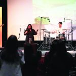 Live band performing on stage with audience in a dimly lit venue.