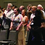 Audience attending a conference, standing and engaged, in a large hall.